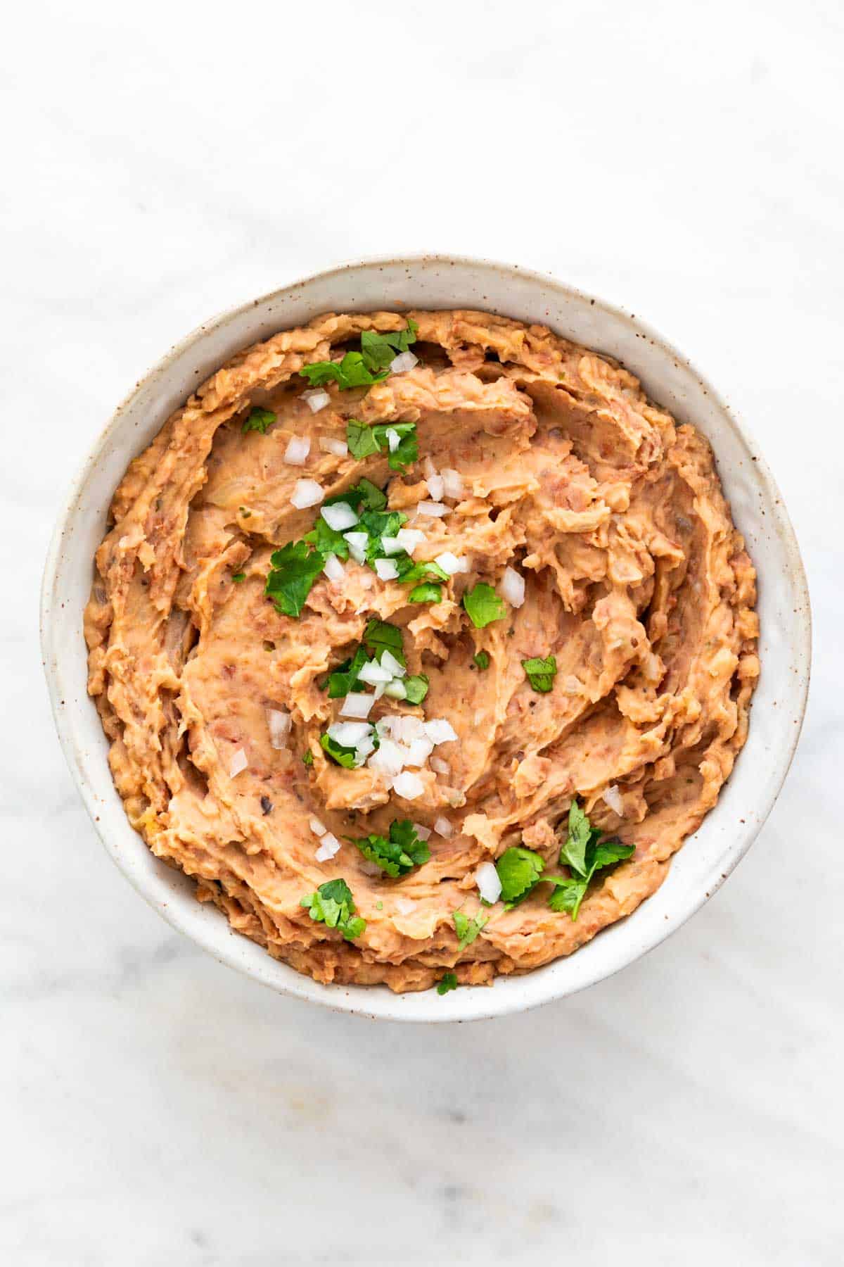 Bowl of vegan refried beans topped with chopped onion and fresh parsley.