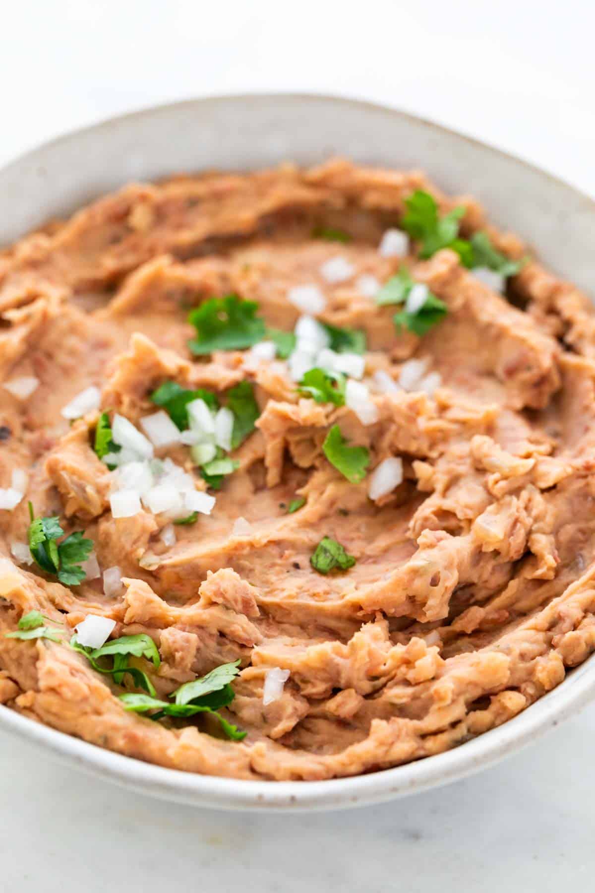 Vegan refried beans in a bowl, garnished with chopped onion and parsley.