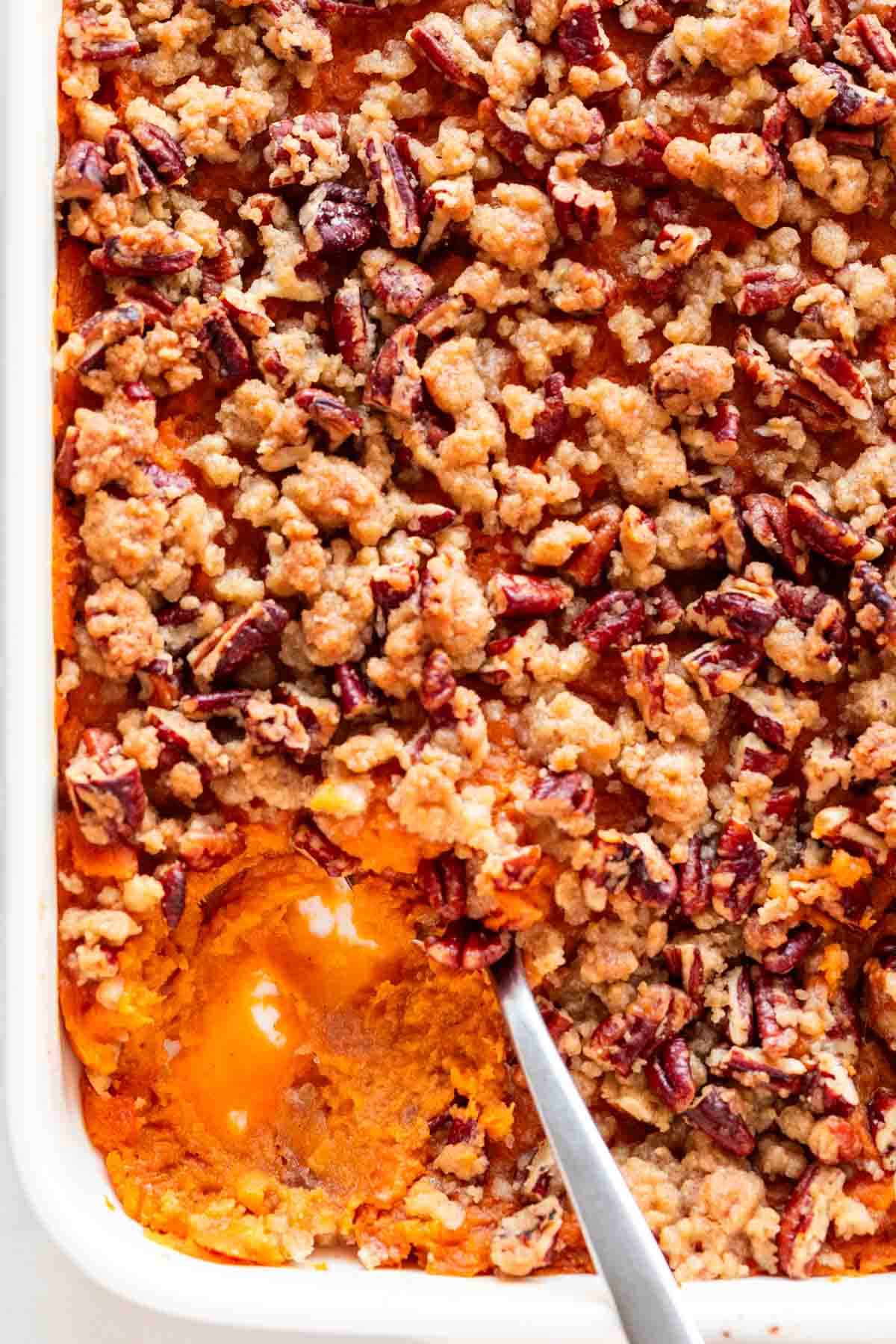 A scoop taken out of vegan sweet potato casserole from a baking dish.