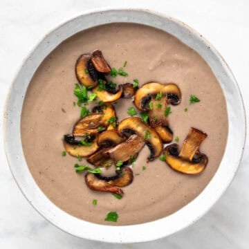 A bowl of vegan mushroom soup garnished with parsley and sautéed mushrooms.