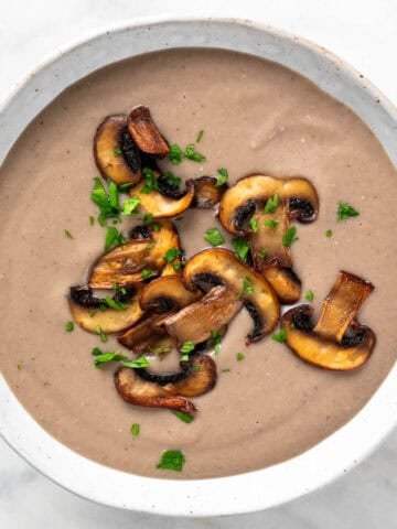 A bowl of vegan mushroom soup garnished with parsley and sautéed mushrooms.