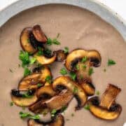 A bowl of vegan mushroom soup topped with sautéed mushrooms and fresh parsley.