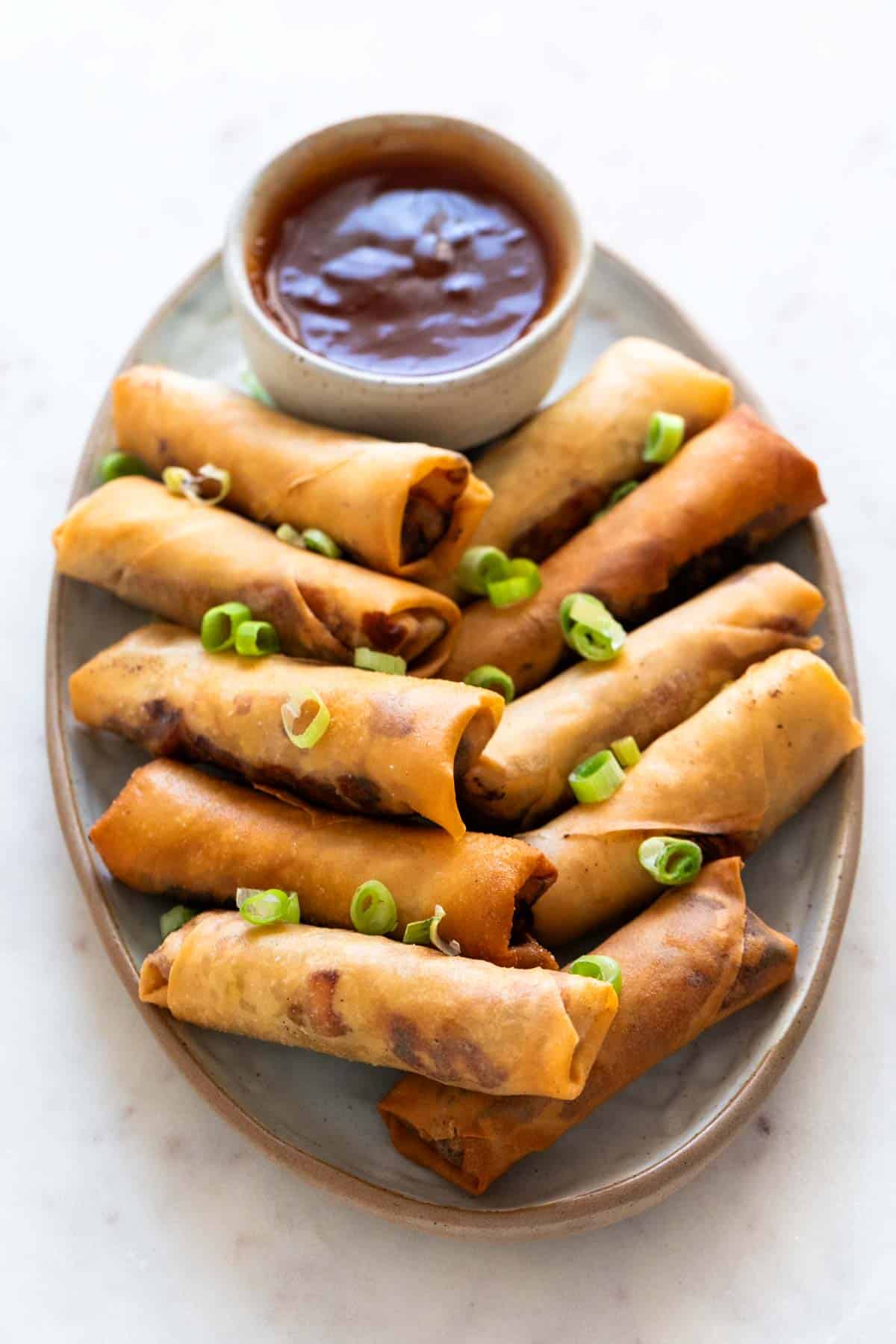 Vegan spring rolls on a plate with sweet and sour sauce garnished with spring onions.