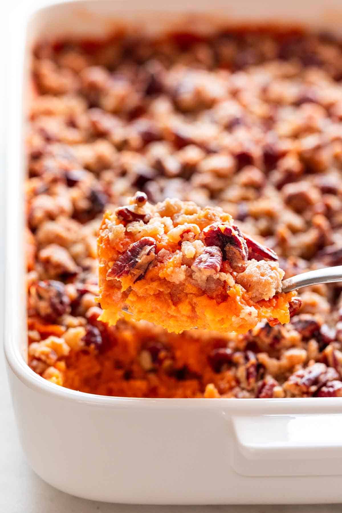 A spoon scooping vegan sweet potato casserole from a baking dish.