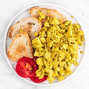 Tofu scramble, bread, and tomato slices arranged in a white dish.