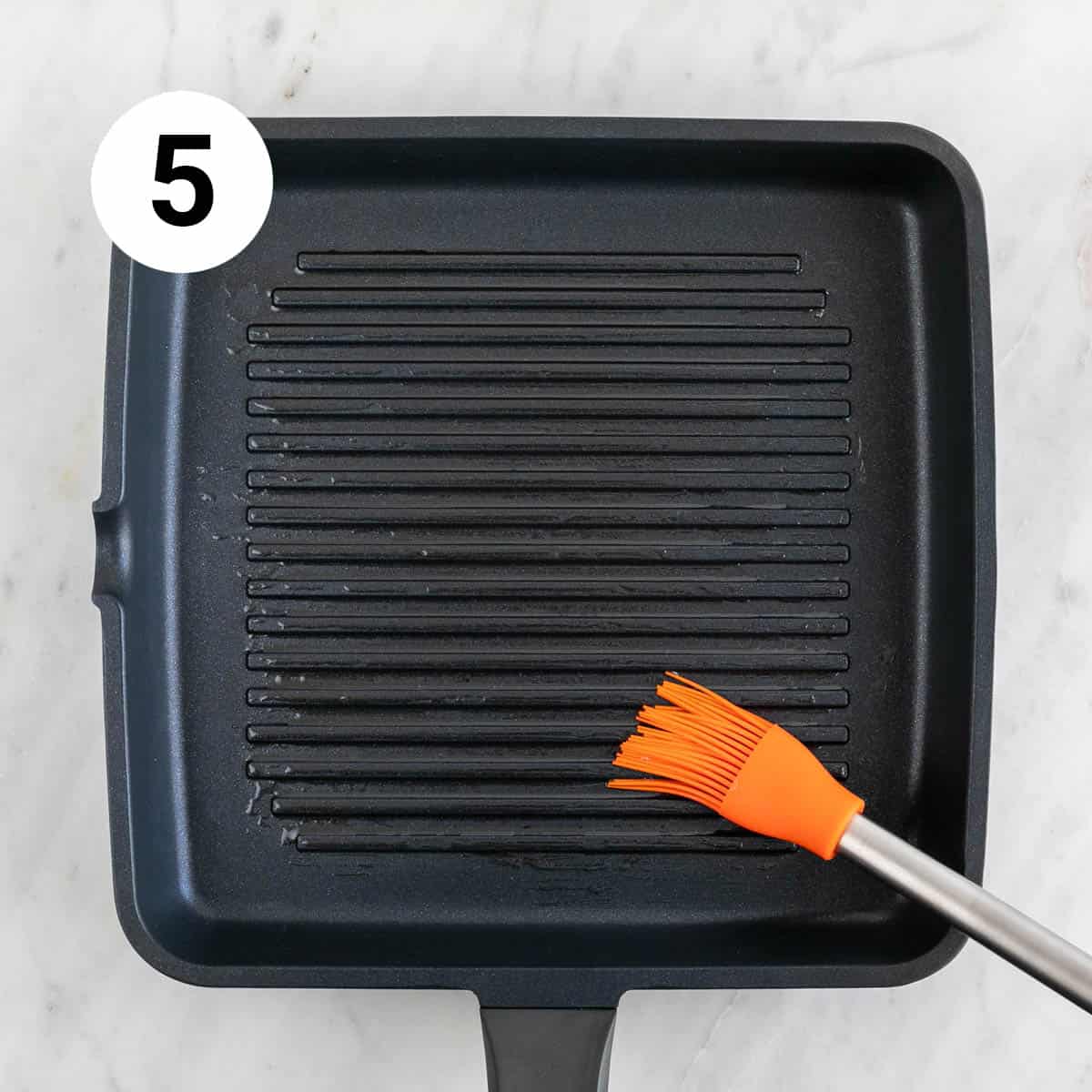 Grill pan being brushed with oil using a brush.