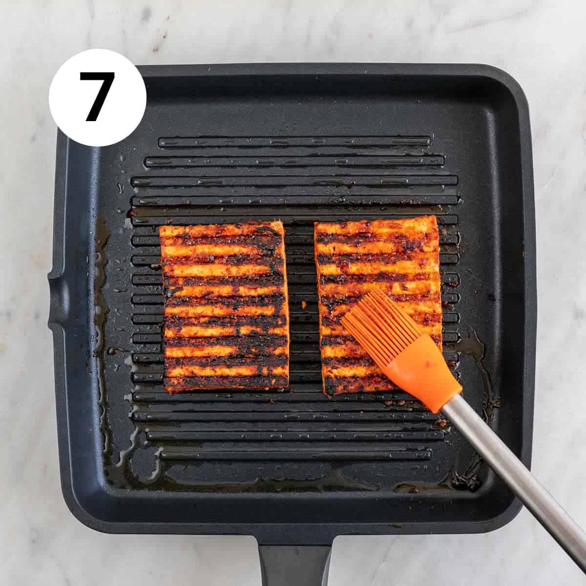 Two tofu steaks in a grill pan being brushed with marinade using a brush.