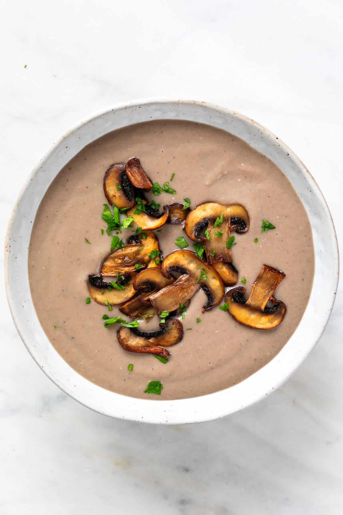 A bowl of vegan mushroom soup topped with sautéed mushrooms and fresh parsley.