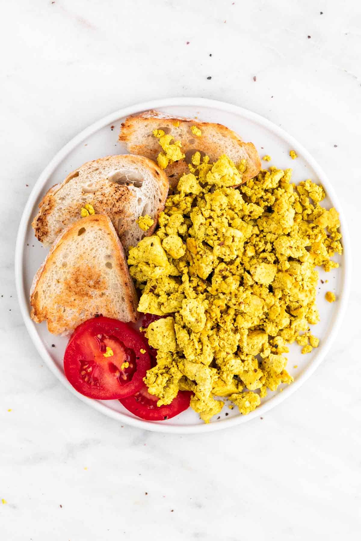 White dish with tofu scramble, bread, and tomato slices.