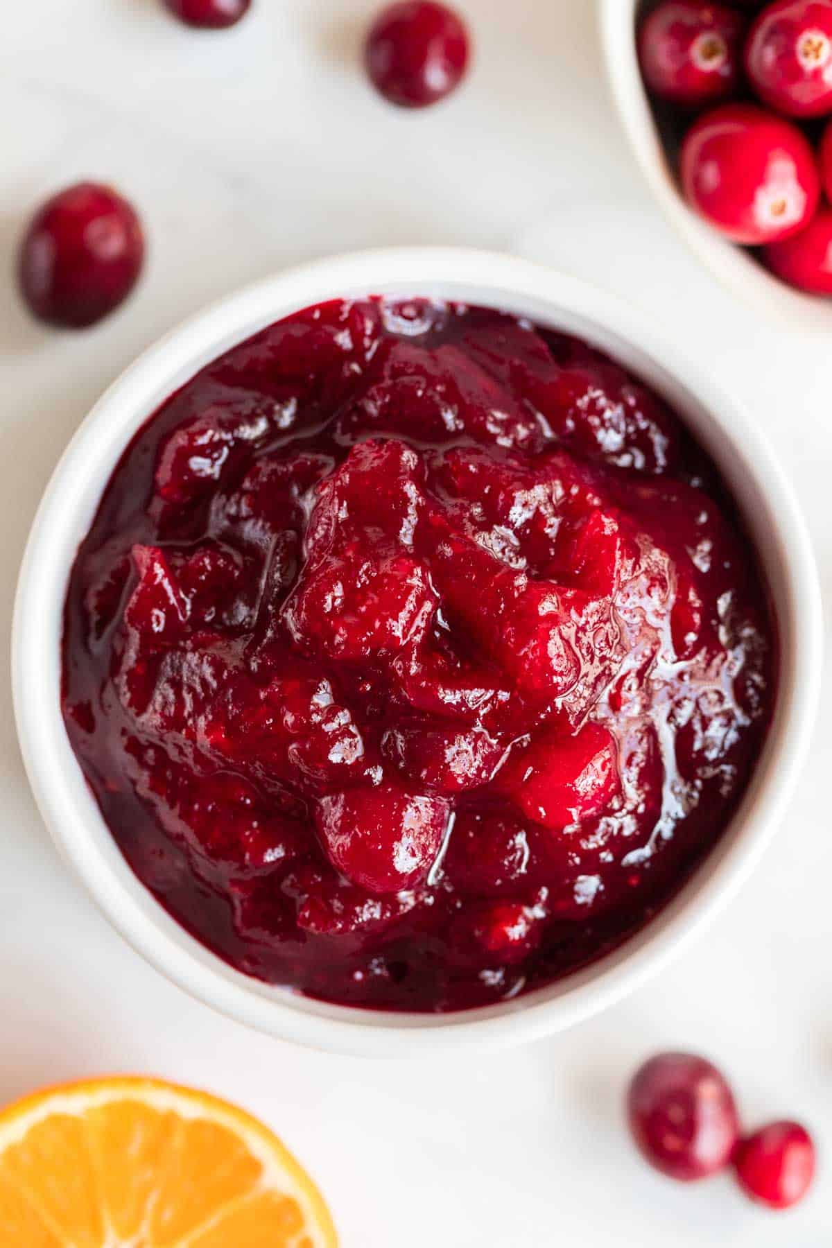 Vegan cranberry sauce in a bowl with fresh cranberries and orange slices around.