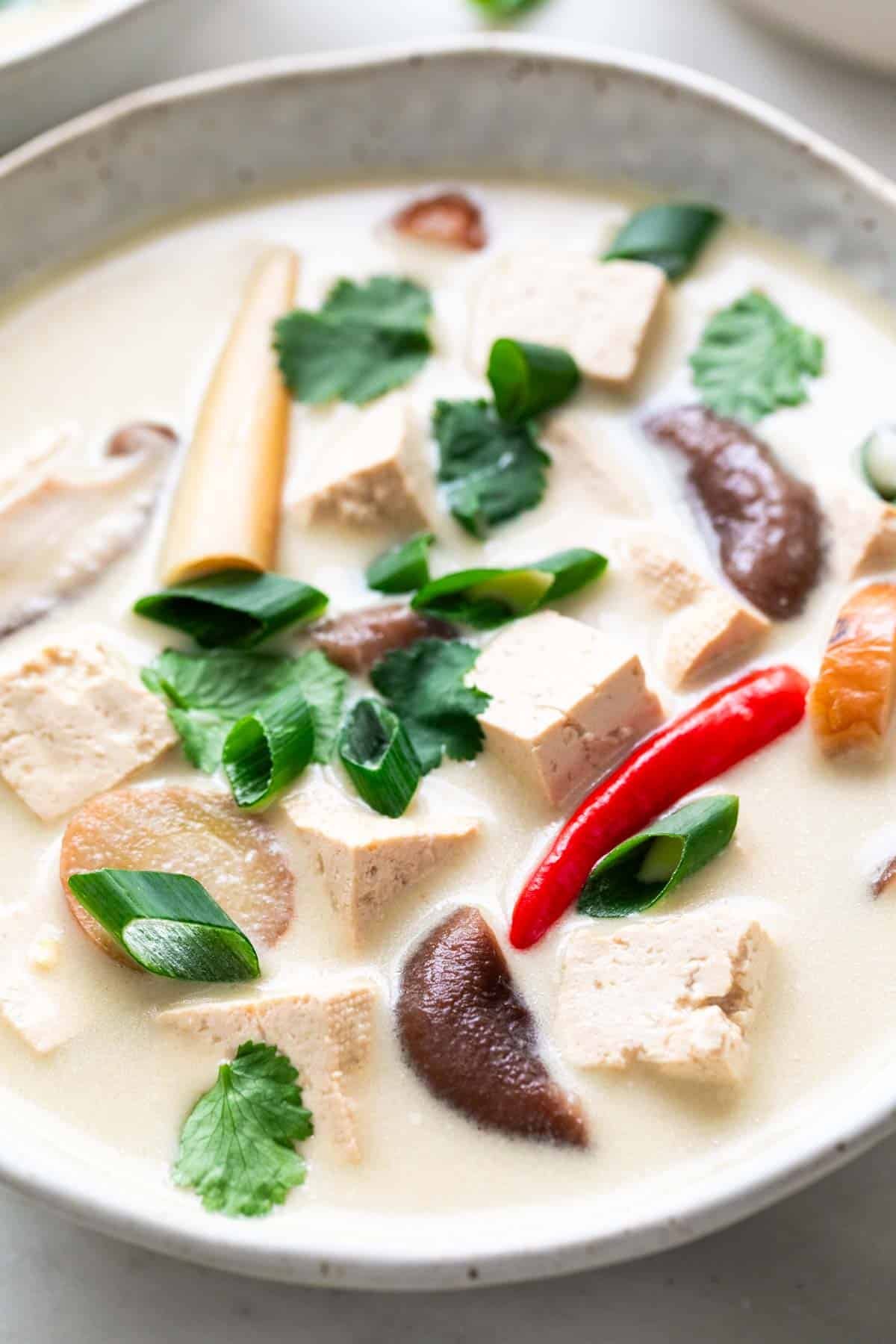 Bowl of vegan tom kha soup topped with green onions and cilantro.