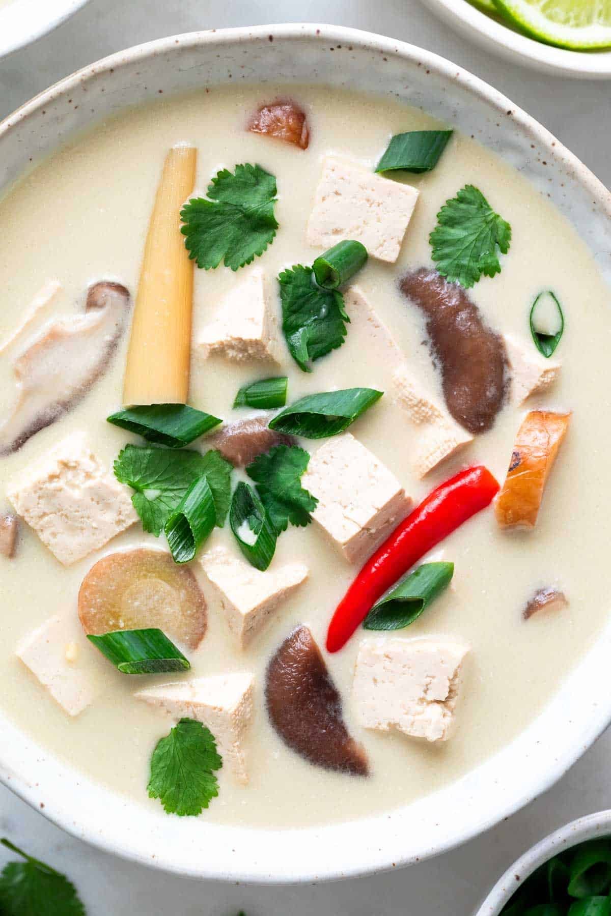 Vegan tom kha soup in a bowl garnished with green onions and cilantro.