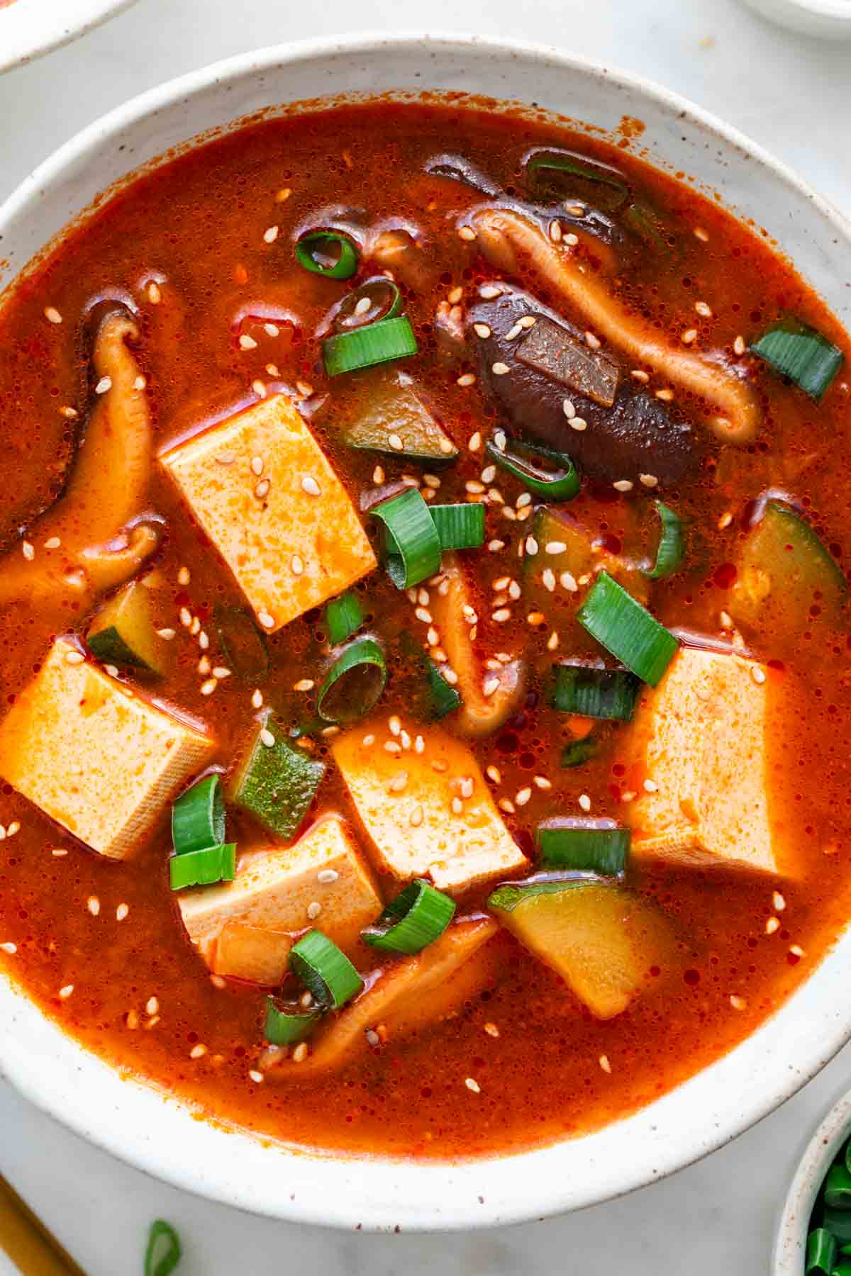 Spicy Korean tofu soup in a bowl, topped with scallions and sesame seeds.