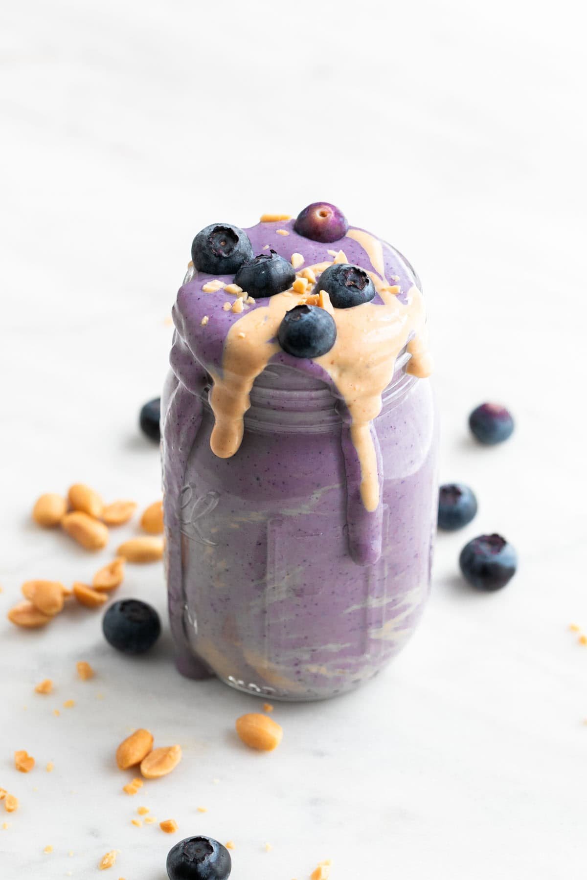 Silken tofu smoothie in a jar with a topping of blueberries, peanut butter, and chopped peanuts.