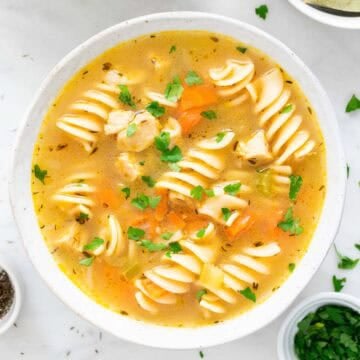 Two bowls of vegan chicken noodle soup garnished with parsley, surrounded by ingredients.