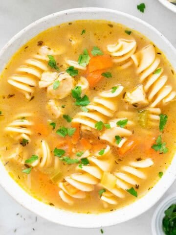 Two bowls of vegan chicken noodle soup garnished with parsley, surrounded by ingredients.