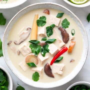 Bowl of vegan tom kha soup garnished with parsley and scallions.