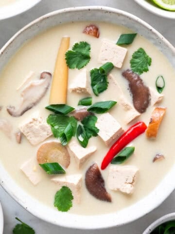 Bowl of vegan tom kha soup garnished with parsley and scallions.