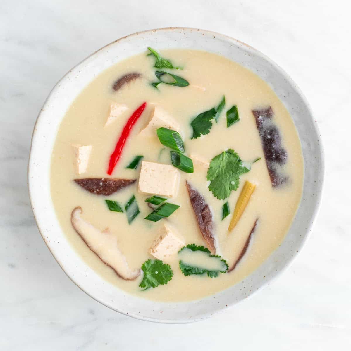 Bowl of vegan tom kha soup topped with fresh parsley and scallions.