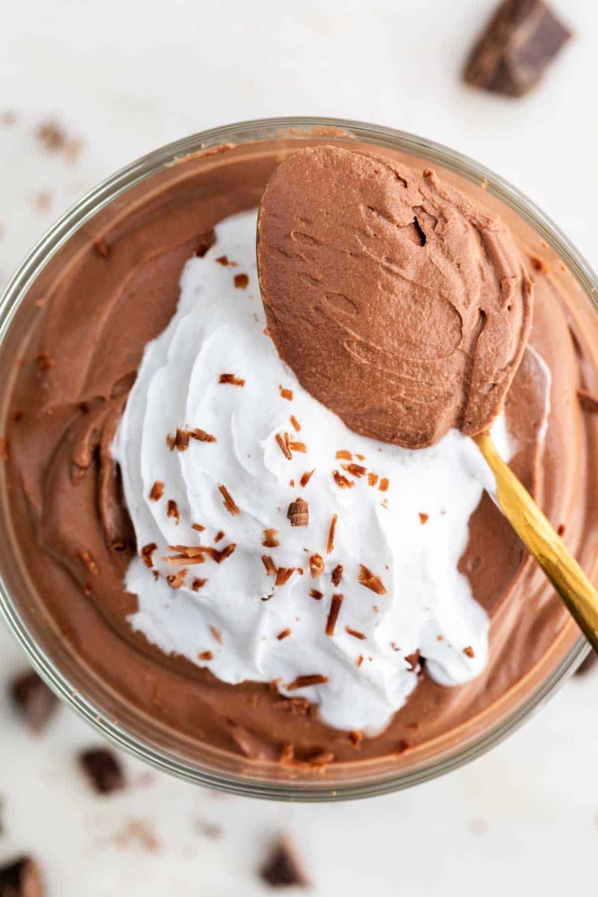 A serving glass of tofu chocolate mousse with a spoonful on top and topped with toppings.