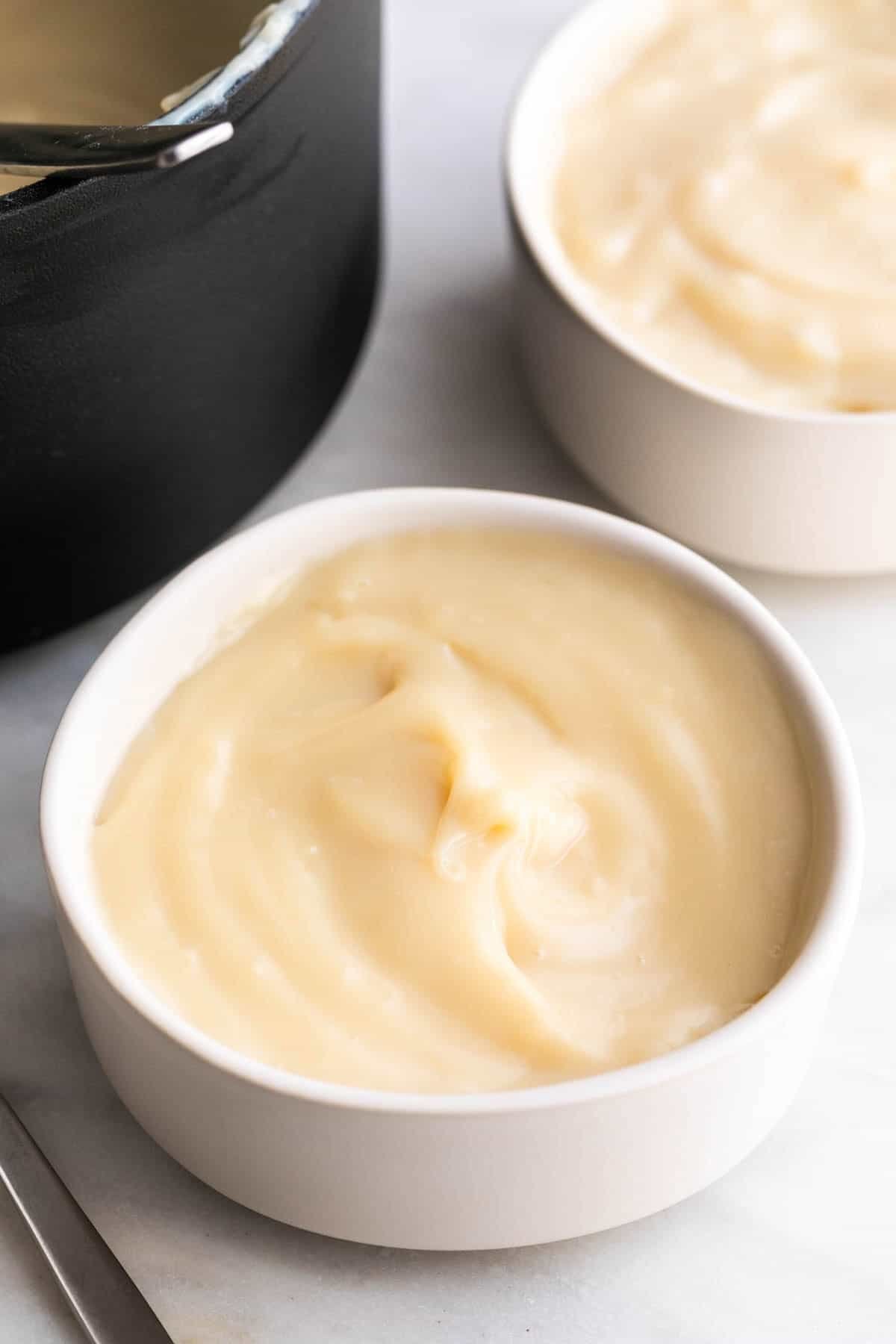 Two bowls of vegan custard with a saucepan in the background.