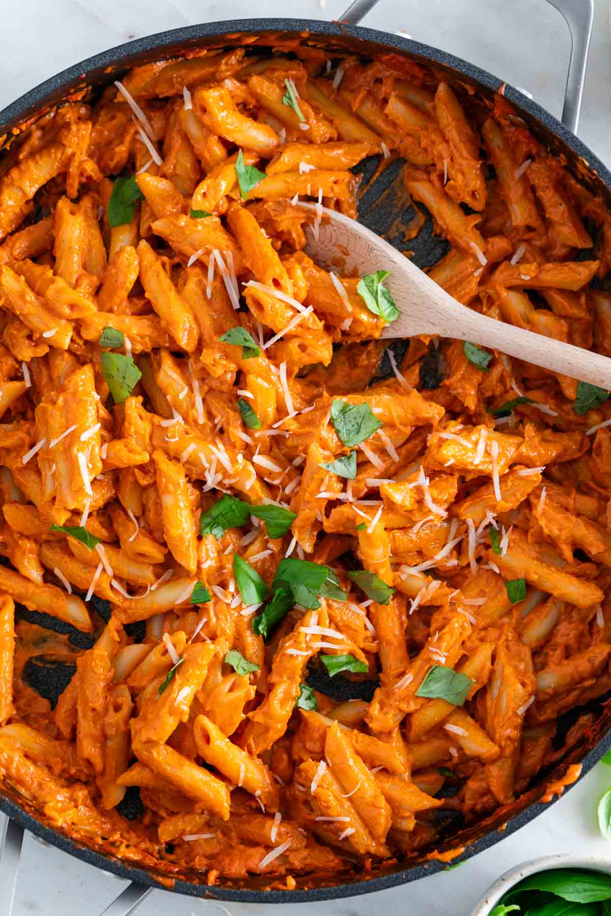 Vegan penne alla vodka in a skillet garnished with basil and vegan parmesan shreds.