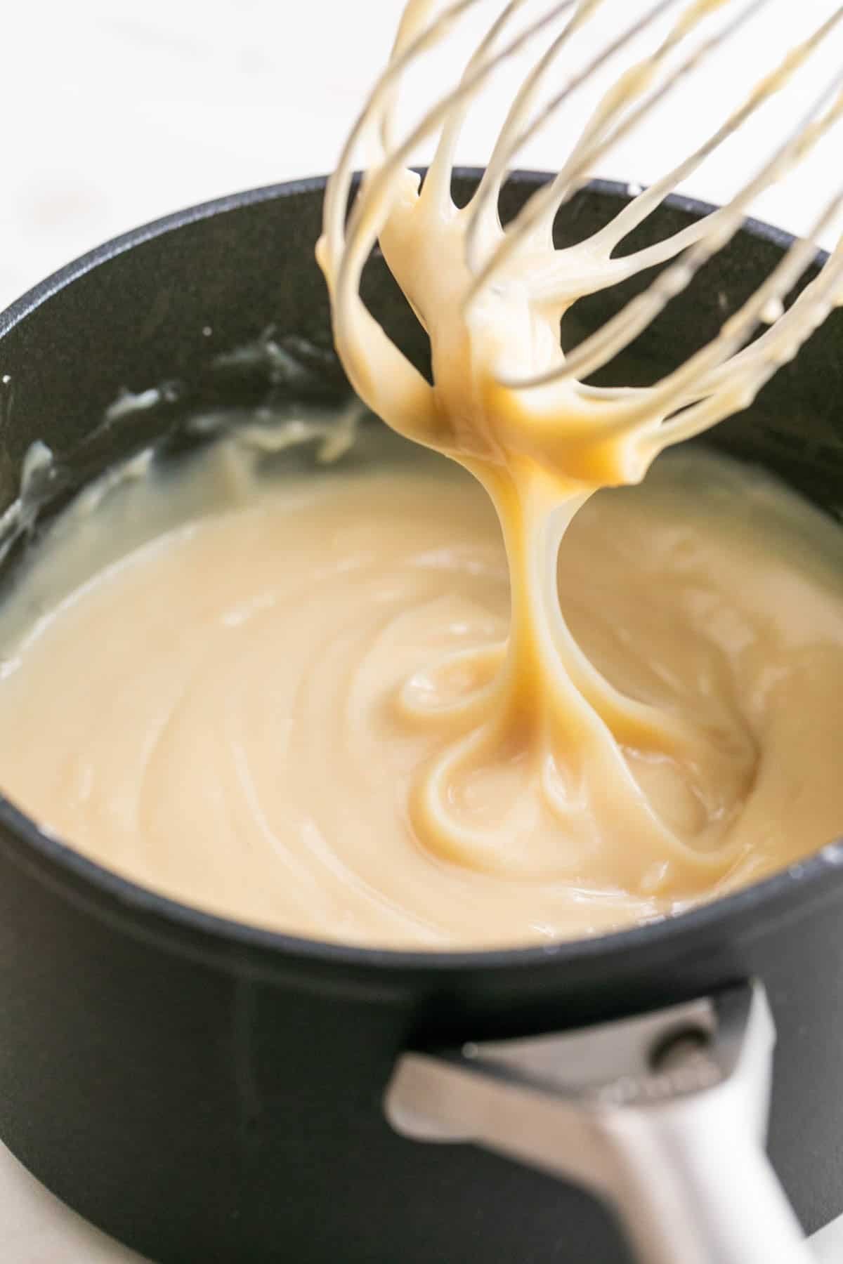 A whisk dripping vegan custard from a saucepan.