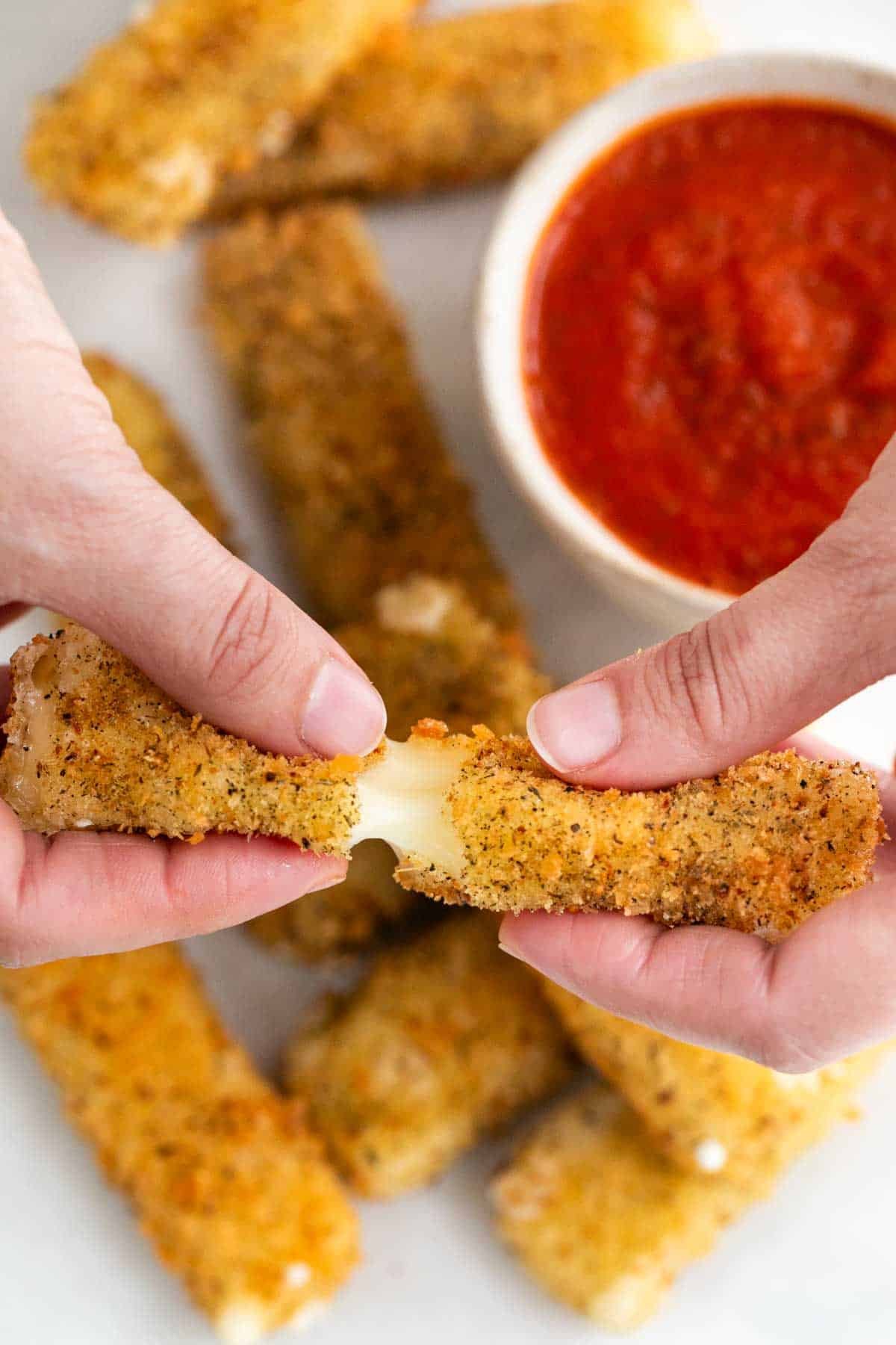 Two hands breaking a vegan mozzarella stick in half.