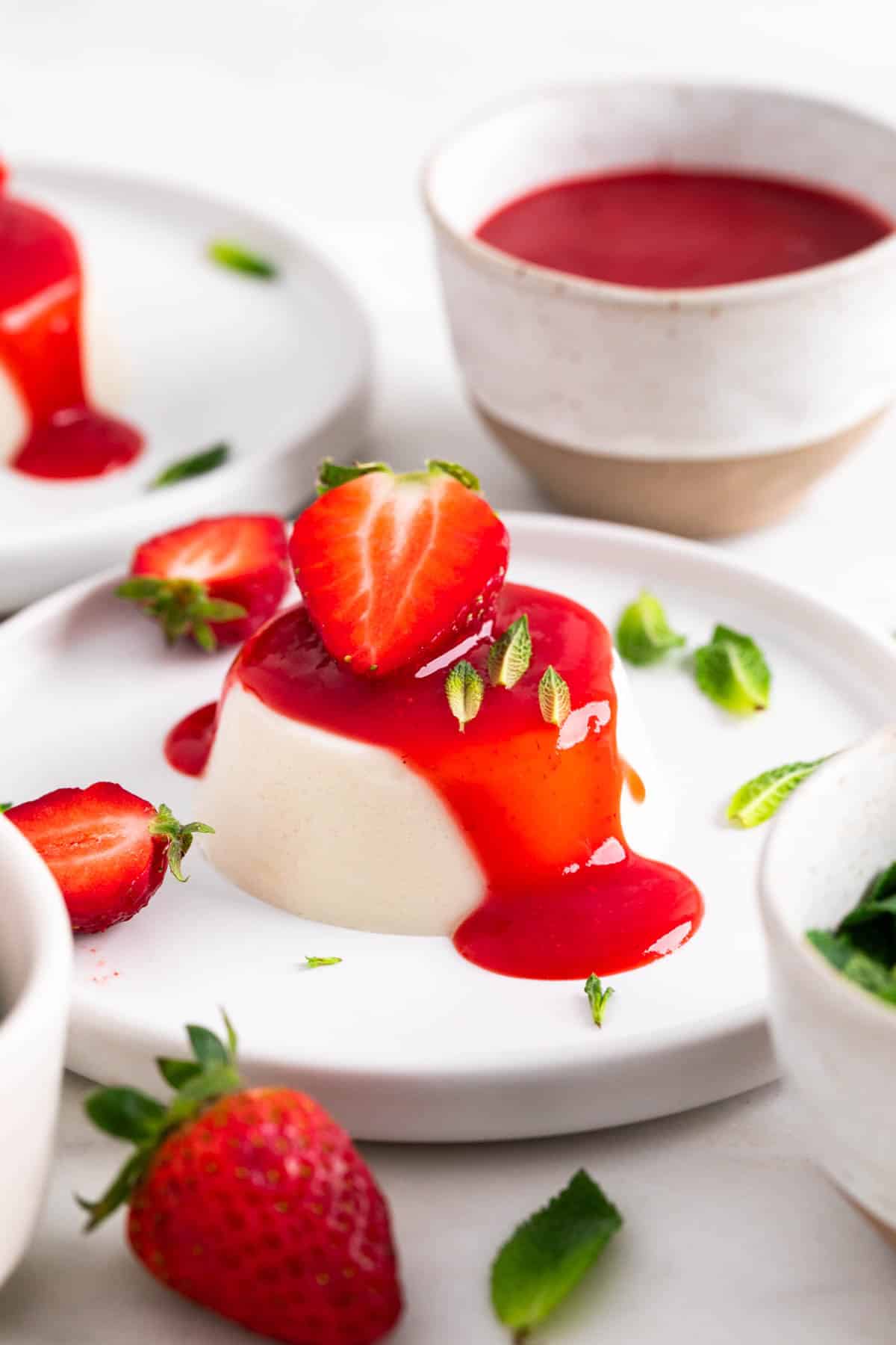 Vegan panna cotta served on a plate with strawberry coulis, a strawberry on top, and mint leaves.