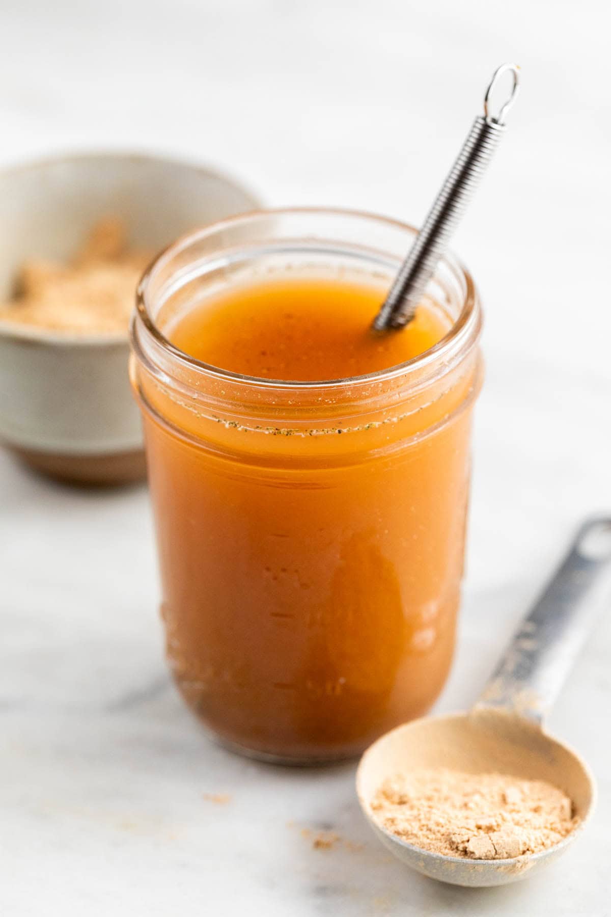 Vegan beef broth in a jar and vegan beef bouillon powder on a spoon.