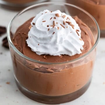 Three serving glasses of tofu chocolate mousse topped with vegan whipped cream and chocolate shavings.