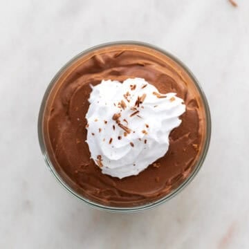 Tofu chocolate mousse in a serving glass with vegan whipped cream and chocolate shavings on top.