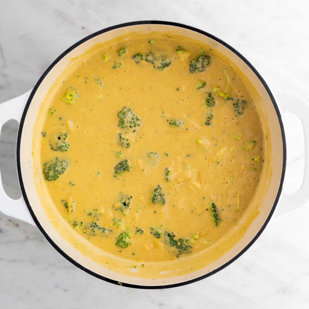 Blended soup in a large pot with broccoli and vegan cheese before cooking.