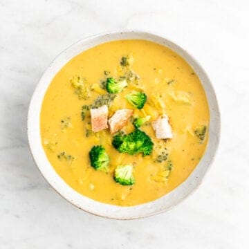 Vegan broccoli cheddar soup in a bowl garnished with bread and vegan cheddar cheese.