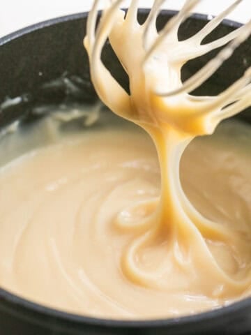 A whisk dripping vegan custard from a saucepan.