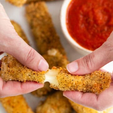 Two hands breaking a vegan mozzarella stick in half.