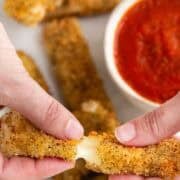 Two hands breaking a vegan mozzarella stick in half.