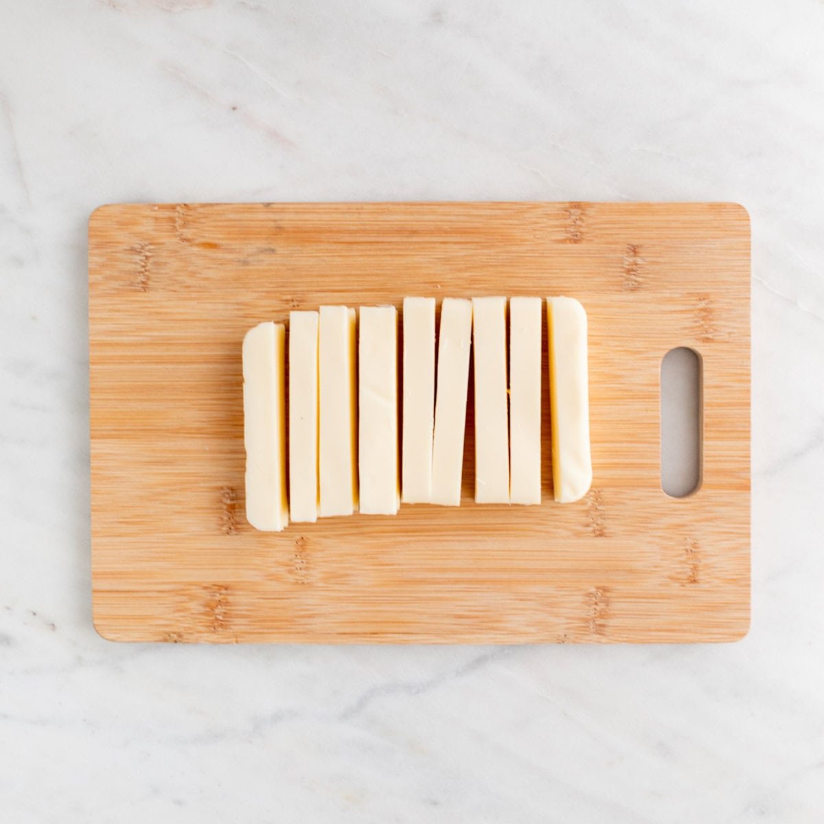 Vegan mozzarella block cut into sticks on a wooden cutting board.