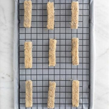 Vegan mozzarella sticks on a wire rack on a lined baking sheet before cooking.