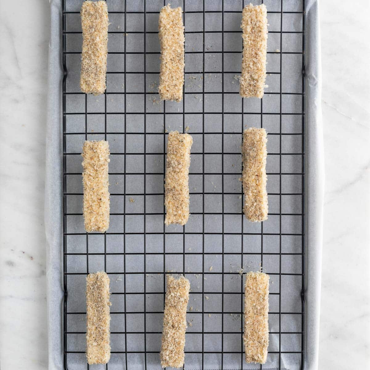 Vegan mozzarella sticks on a wire rack on a lined baking sheet before cooking.