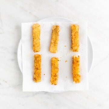 Fried vegan mozzarella sticks on a plate with paper towels.