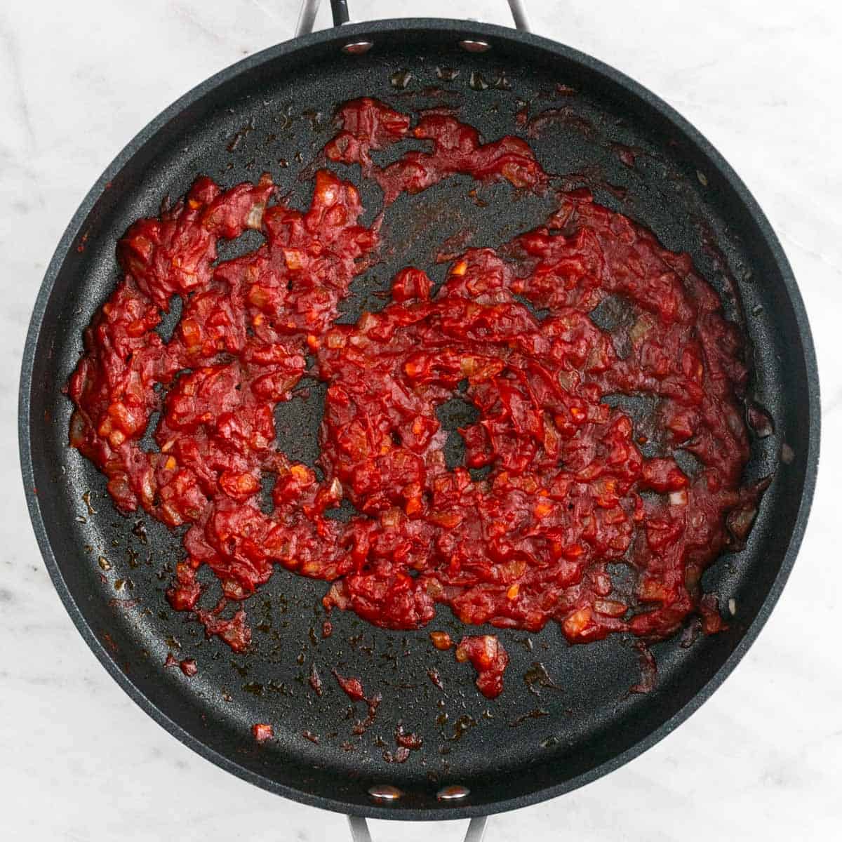 Sautéed onion and garlic with tomato paste, salt, and pepper in a skillet.