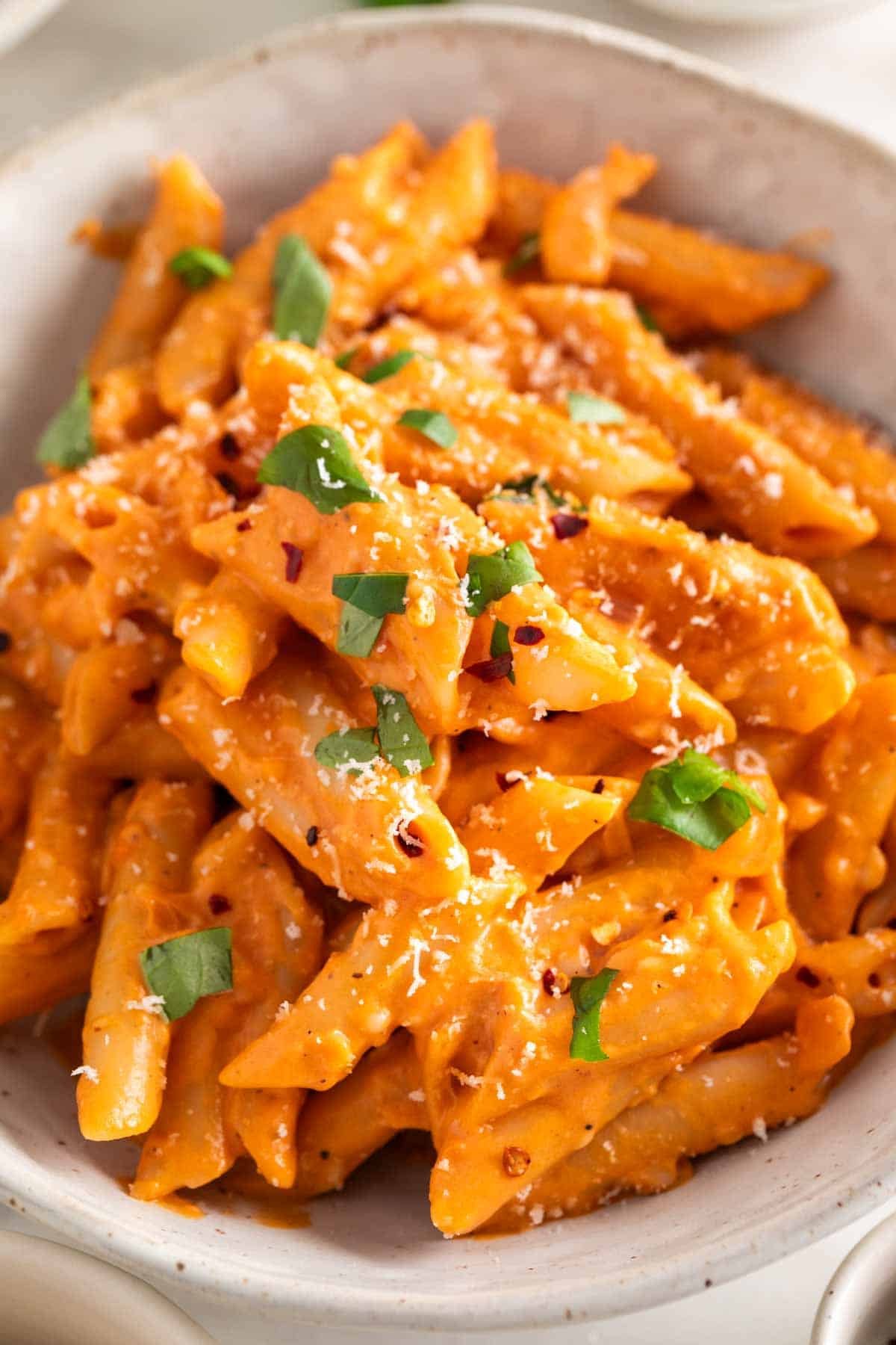 Penne with vegan pasta sauce in a bowl, topped with fresh basil and vegan Parmesan.