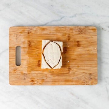 Tofu filet chopped into chicken breast shapes on a wooden cutting board.