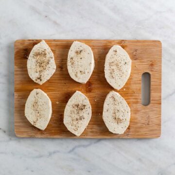 6 tofu filets seasoned with salt and pepper on a wooden cutting board.