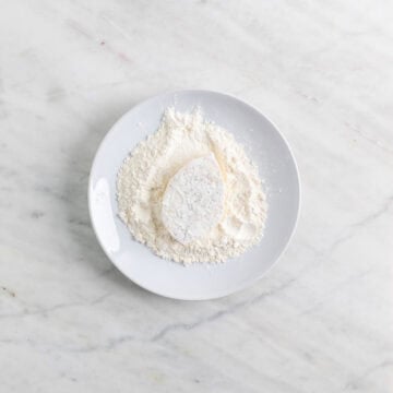 Tofu filet being coated in flour on a plate.