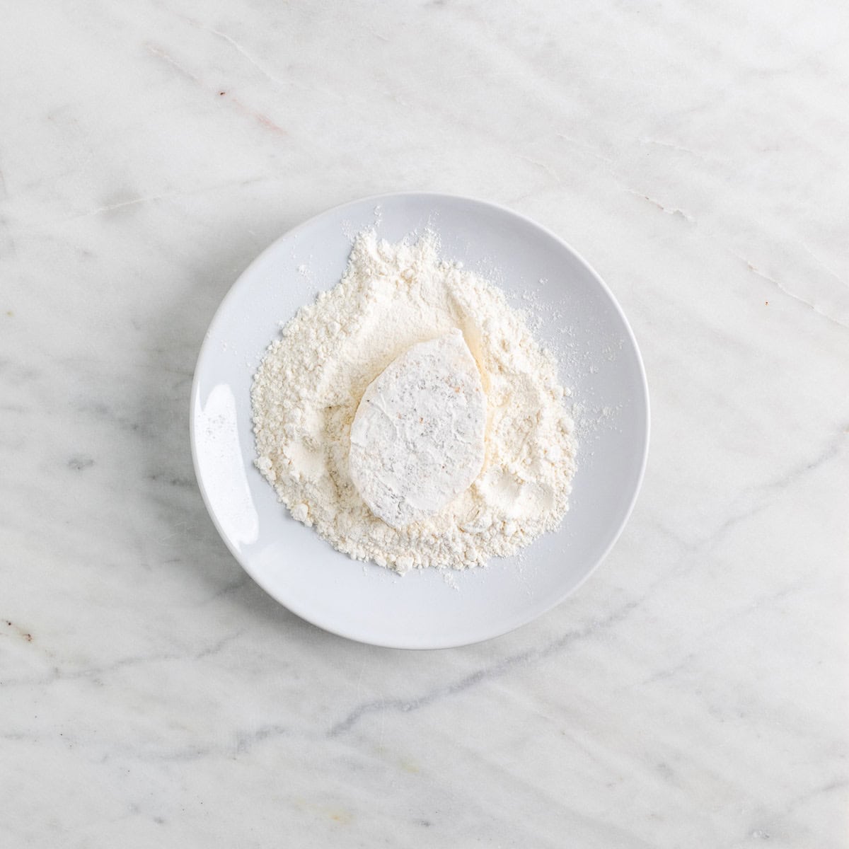 Tofu filet being coated in flour on a plate.