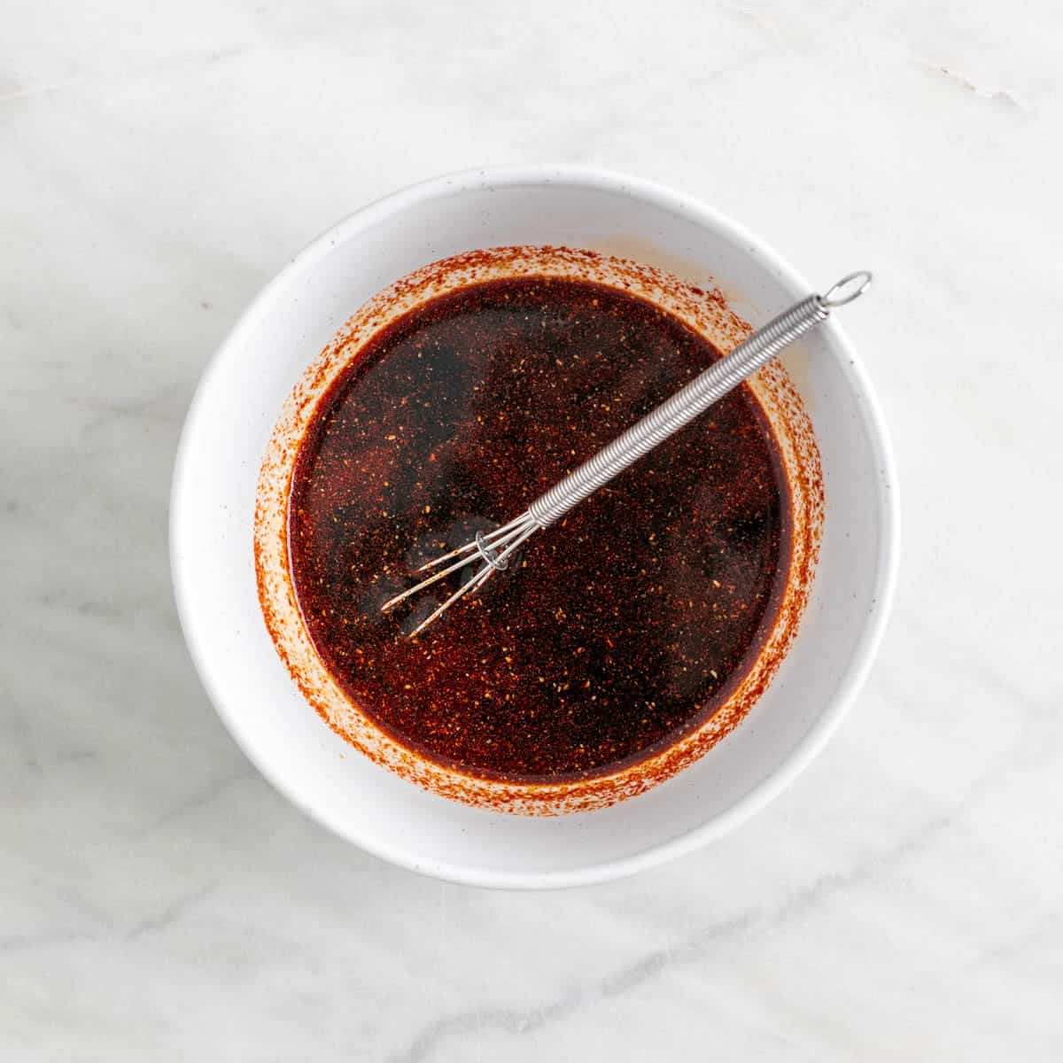 Marinade in a bowl with a mini whisk.