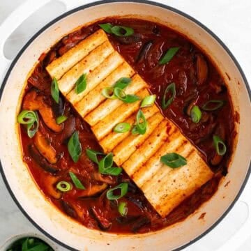 Vegan kimchi stew in a large pot with scallions on top, and a bowl of extra scallions on the side.