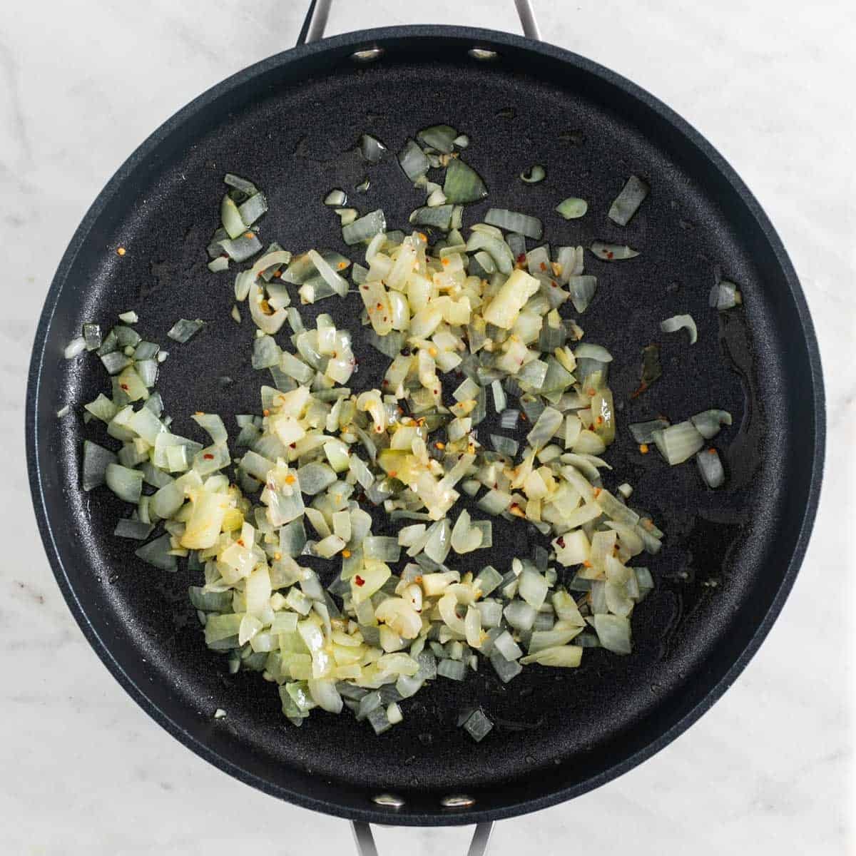 Sautéed onion and garlic in a skillet with red pepper flakes.